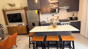 Una cocina moderna con una isla central, taburetes de bar, horno empotrado, microondas y un televisor montado en la pared.