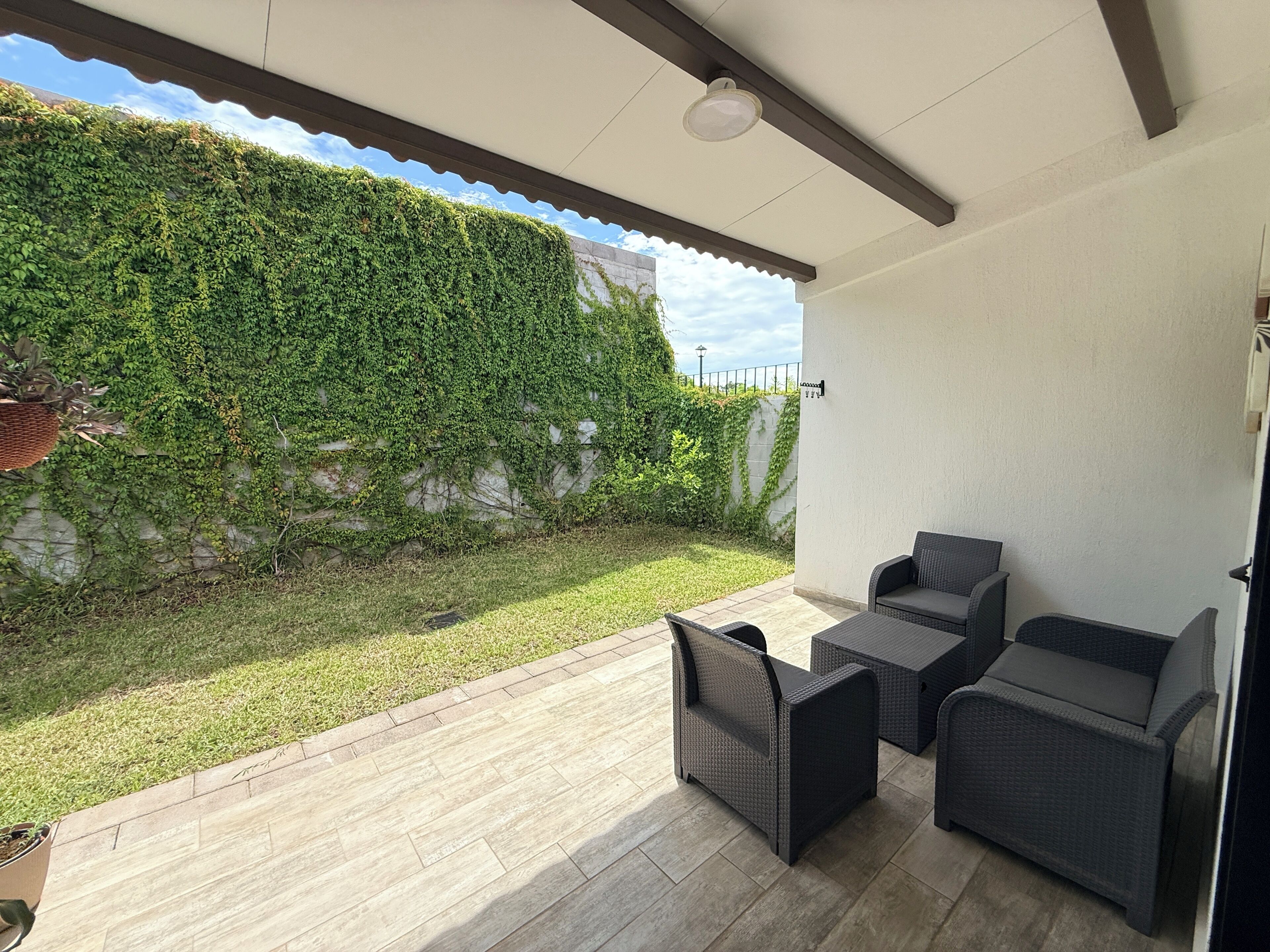 Un patio couvert aménagé avec des sièges et un mur recouvert de verdure.