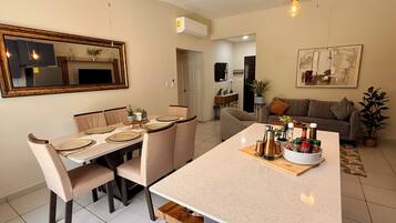 Une cuisine moderne dotée d’un îlot central, d’un coin repas avec des chaises, de ventilateurs de plafond et d’un salon avec un canapé.