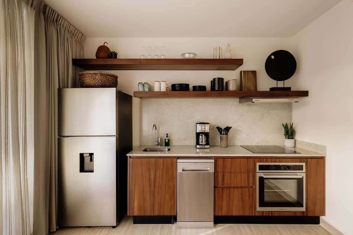 Cocina compacta equipada con refrigerador, lavavajillas, horno y gabinetes de madera.