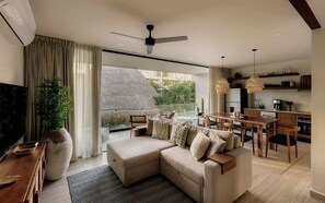 A modern living room with a sofa, a TV, a large plant, and a dining area with a table and chairs.