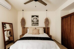 Ein Schlafzimmer mit einem Bett, einem Holz-Kopfteil, Pendelleuchten, einem Spiegel und einem Kleiderschrank.