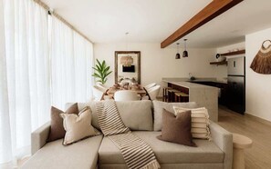 A modern living room with a sofa, a dining table, and a kitchen area.