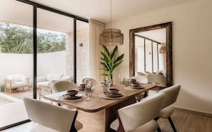 A dining area with a wooden table set for four, surrounded by chairs, with a large mirror and a hanging light fixture.