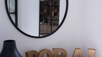 A round mirror on a wall, a dark vase, and wooden letters spelling "DORAL welcome" on a wooden surface.