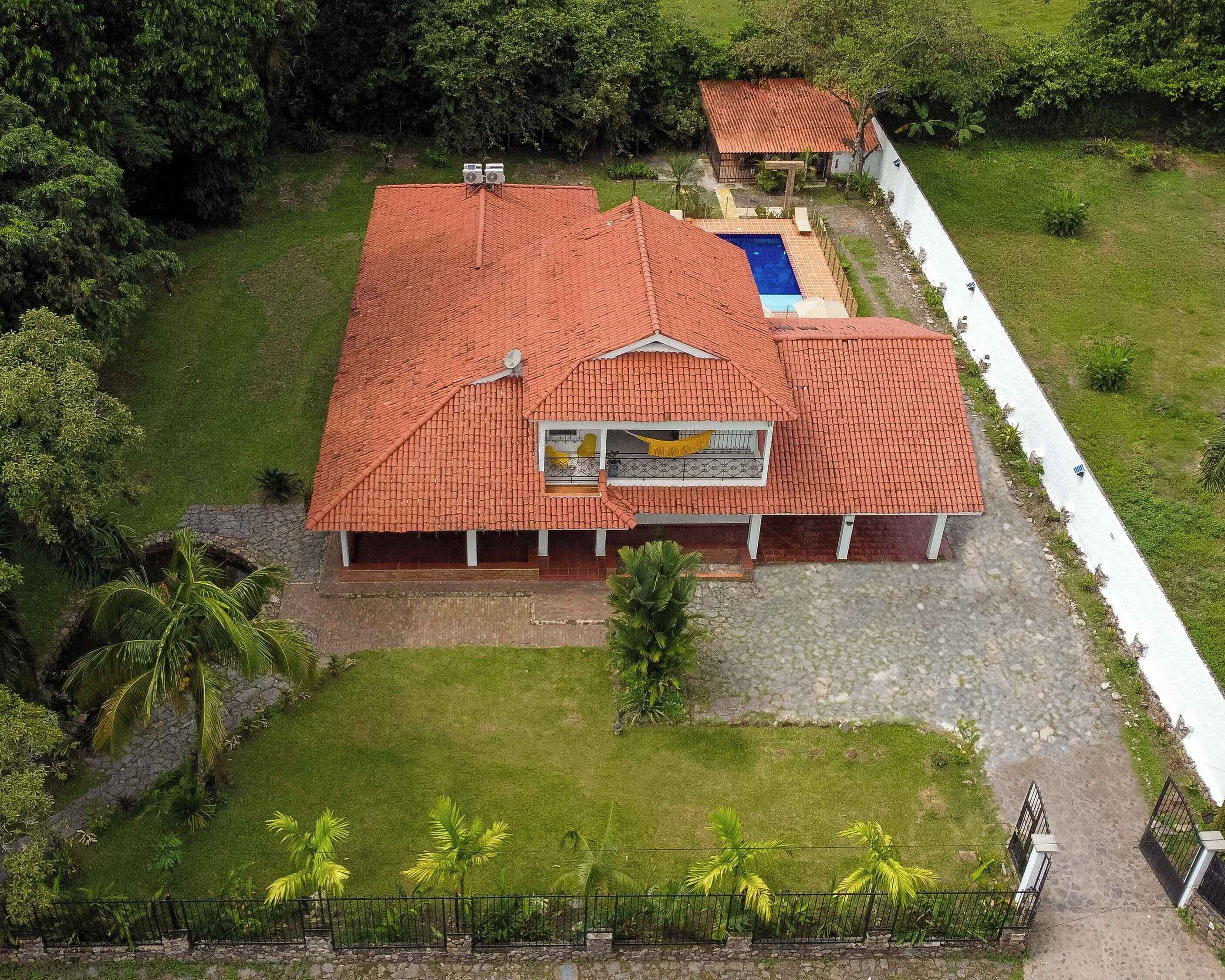 A large building with a red-tiled roof, a swimming pool, and a fenced garden area.