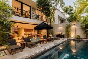 A modern house with a pool, outdoor seating, and a staircase leading to a balcony.