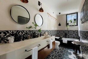 A bathroom with a large mirror, a sink, a bathtub, and a window with plants. - Casa Chacalaca Perfect Bachelorette Villa (Tulum)