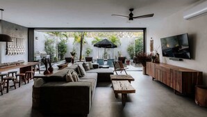 A modern living room with a sofa, chairs, a coffee table, a TV, and a ceiling fan. - Casa Chacalaca Perfect Bachelorette Villa (Tulum)