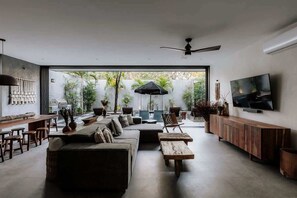 A modern living room with a sofa, chairs, a coffee table, a TV, and a ceiling fan. - Casa Chacalaca Perfect Bachelorette Villa (Tulum)