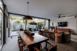 Une cuisine moderne avec une longue table en bois, des tabourets de bar et un téléviseur fixé au mur.