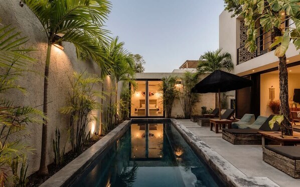 A pool area with lounge chairs, a small pool, and a building with a balcony.