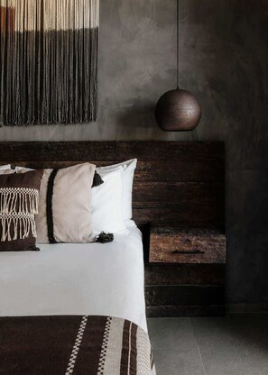A bedroom with a bed, a hanging light, and a wooden nightstand.
