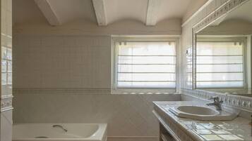 A bathroom with a bathtub, a sink, and a window with blinds.