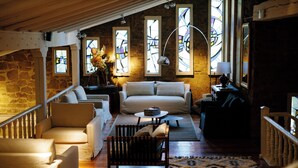 A cozy living room with a stone wall, a wooden ceiling, and large stained glass windows. - Hotel Finca El Peregrino (Puente La Reina)