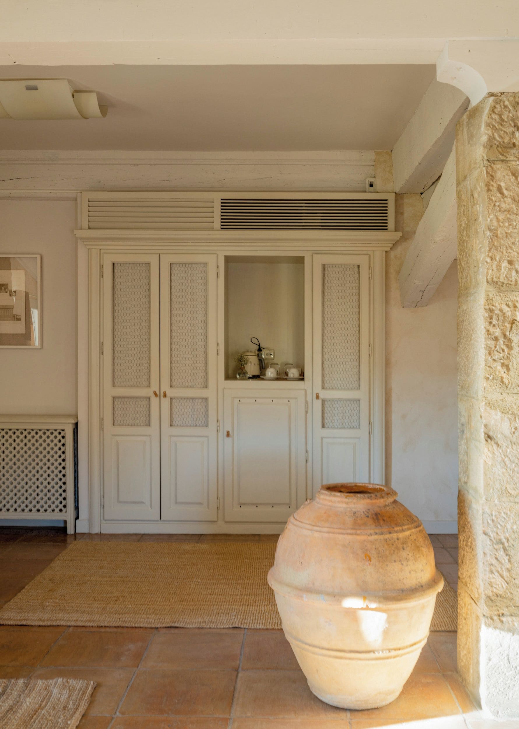 Una habitación con una maceta de barro grande, un armario blanco con puertas de cristal y un radiador en la pared.
