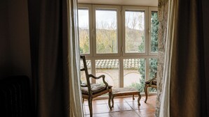 Una habitación con un ventanal grande, una silla de madera y un pilar de piedra.