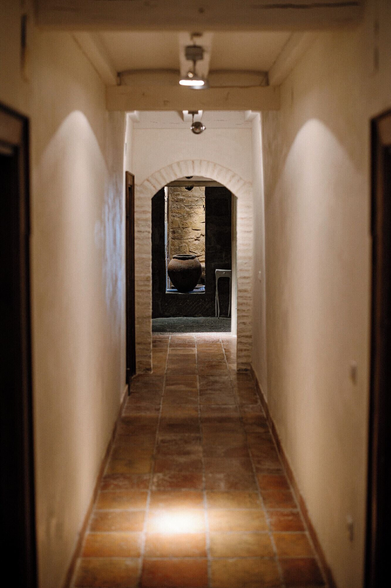 A narrow hallway with a tiled floor, a stone wall, and a door at the end.
