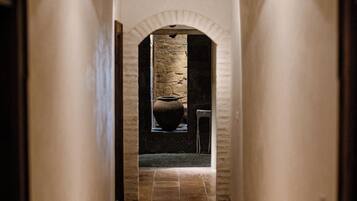 A narrow hallway with a tiled floor, a stone wall, and a door at the end.