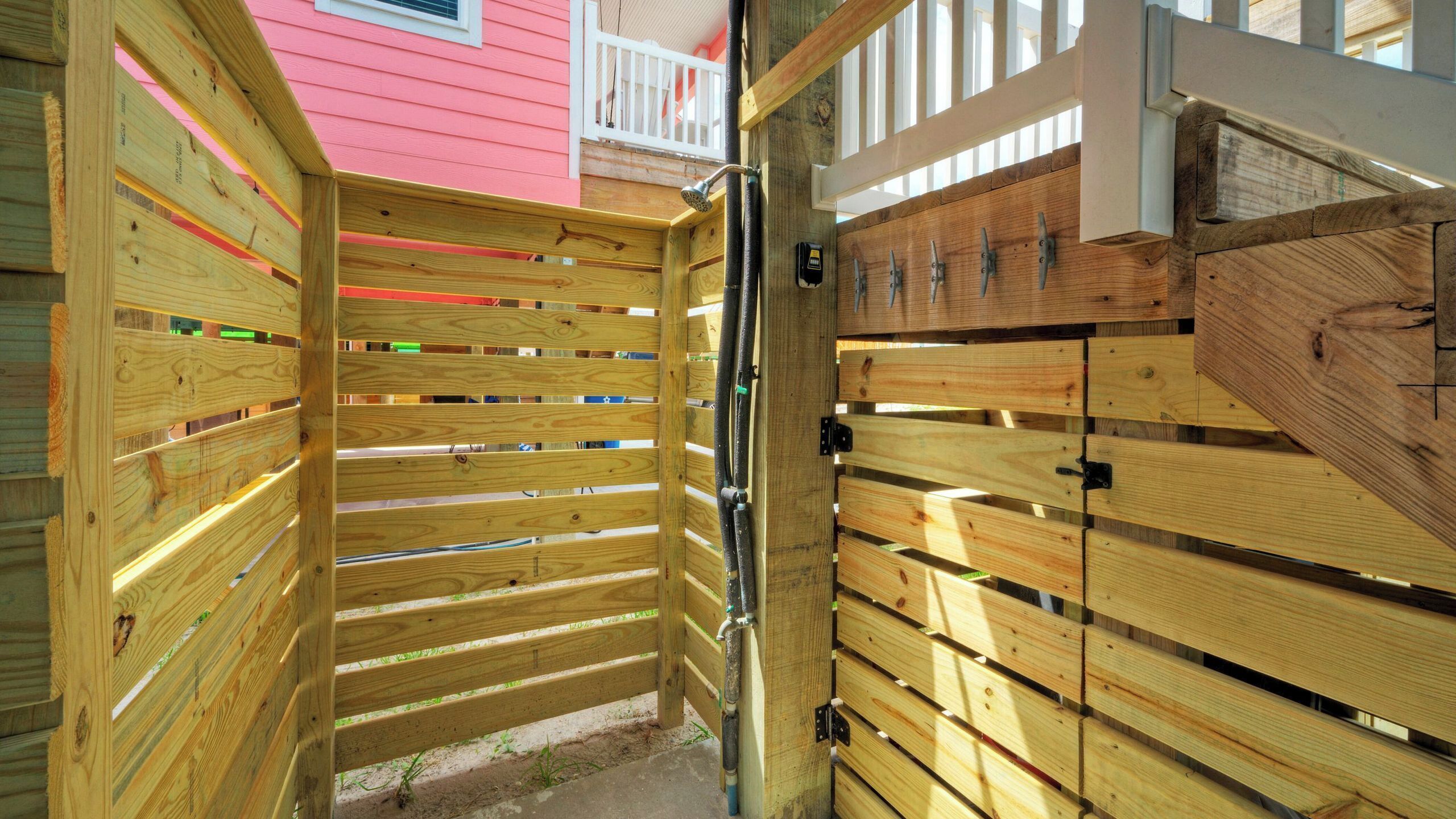 Une porte en bois avec un loquet métallique, une clôture en bois et, au fond, un bâtiment rose.