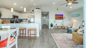 A modern kitchen with white cabinets, a central island, and a dining area with a table and chairs. - Salty Texan by Avantstay Central Location, Views (Port Aransas)