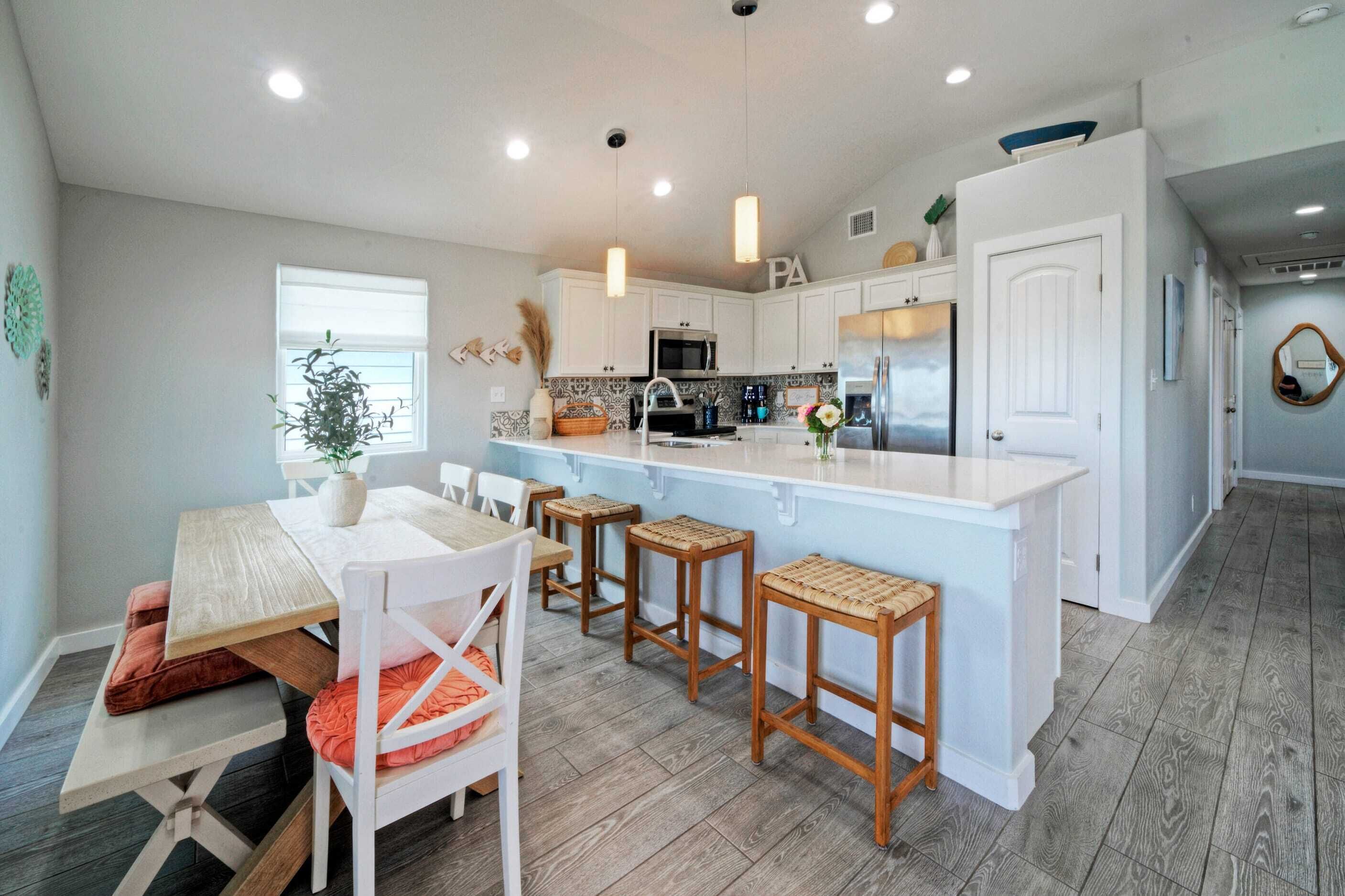 A modern kitchen with white cabinets, a central island with stools, and a dining area with a wooden table and chairs.