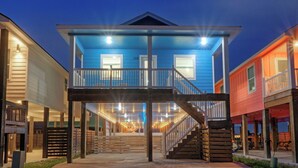 A two-story building with a balcony, a staircase, and a covered outdoor area with string lights. - Salty Texan by Avantstay Central Location, Views (Port Aransas)