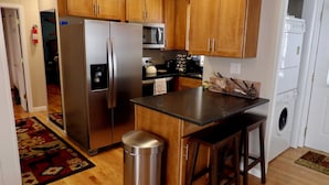 A kitchen with wooden cabinets, stainless steel appliances, a trash can, and a bar stool. - Tranquility Beech: 2BR Condo Steps from the Resort--Parking Lot Level: No Stairs (Banner Elk)