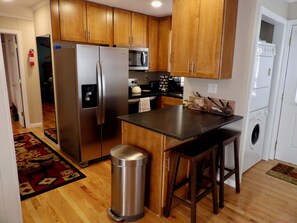 A kitchen with wooden cabinets, stainless steel appliances, a trash can, and a bar stool.