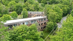 A two-story building with a stone facade and multiple balconies, surrounded by dense forest. - Tranquility Beech: 2BR Condo Steps from the Resort--Parking Lot Level: No Stairs (Banner Elk)