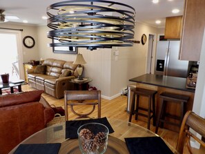 A modern kitchen with a stainless steel refrigerator, a dining area with a glass table, and a leather sofa.