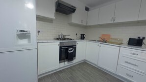 A modern kitchen with white cabinets, a built-in oven, a dishwasher, and a water dispenser. - Spacious 4BR Bungalow with Parking Near Spider-Man Filming Locations (London)