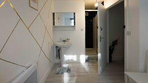A narrow hallway with a white sink, a mirror, and a door leading to a bathroom. - Spacious 4BR Bungalow with Parking Near Spider-Man Filming Locations (London)