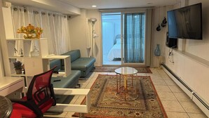 A modern living room with a sofa, a small table, a TV, and a view of a bedroom through a glass door. - 2-bedroom, 1 Bath apartment in gorgeous Roslyn with Washer Dryer in unit (Roslyn)