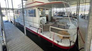 Un bote cubierto con zona de cubierta, asientos y un espacio cerrado pequeño con ventanas.