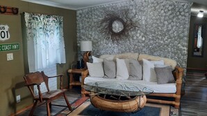 Un salon comprenant un canapé, une table basse en verre, une chaise en bois, une lampe et un élément décoratif mural.