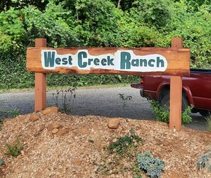 Une enseigne en bois portant l’inscription « West Creek Ranch » dans un style rustique.