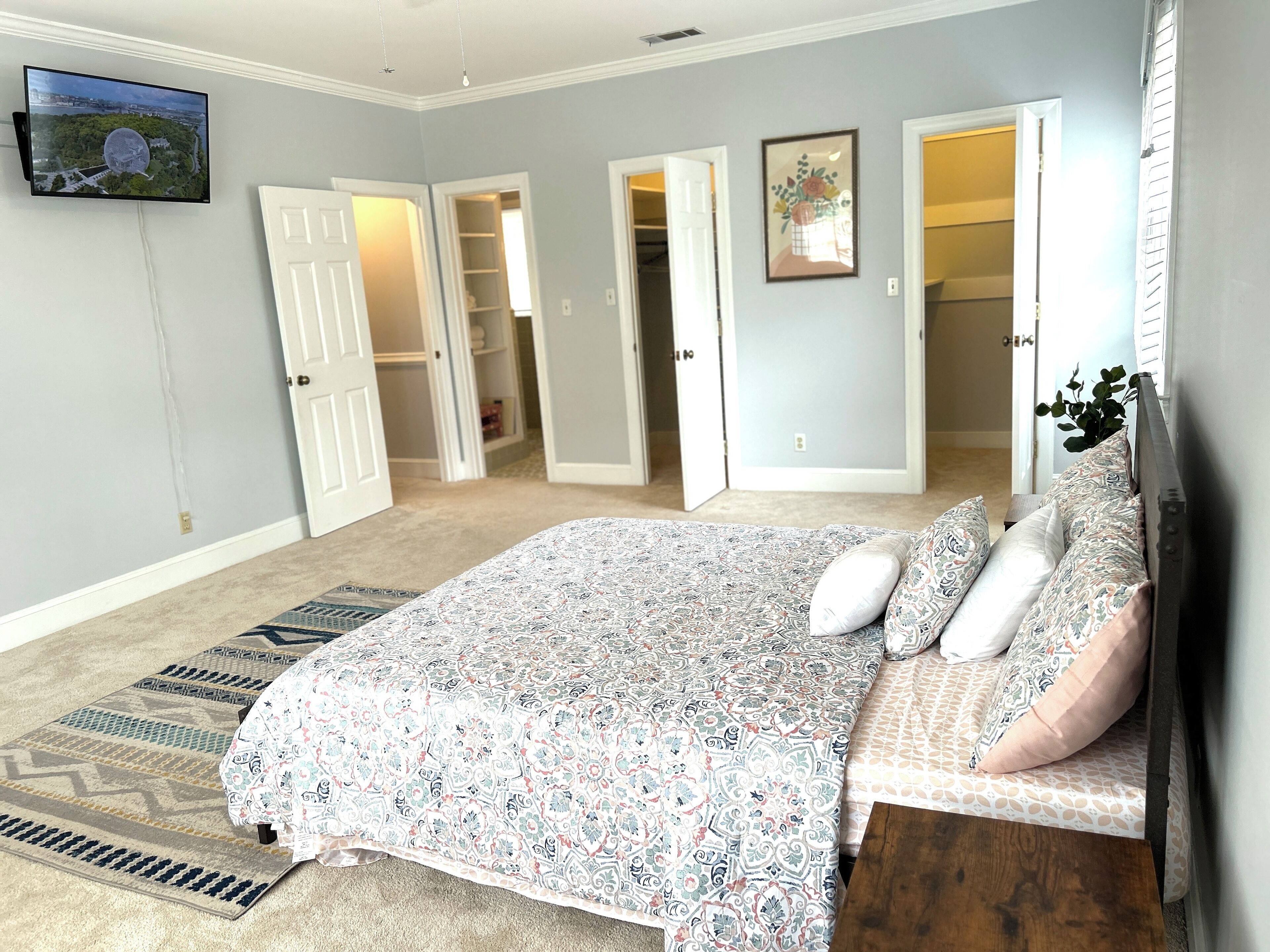 Un dormitorio con una cama grande, un televisor montado en la pared y un armario con las puertas abiertas.