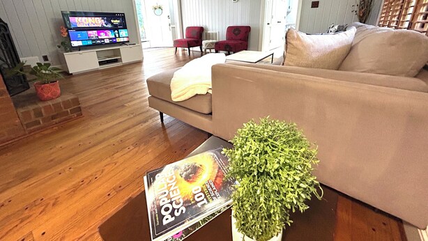 Ett vardagsrum med en beige soffa, ett soffbord med ett tidningsnummer, en tv på ett tv-bord och en röd fåtölj.