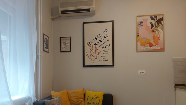 A living room with a black sofa, yellow and grey cushions, a framed artwork, and a radiator. - centrocentro (Novi Sad)