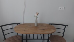 A round wooden table with two cushioned chairs, a vase with flowers, and a power outlet on the wall. - centrocentro (Novi Sad)