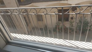 A balcony with a metal railing, potted plants, and a view of a building with a tiled wall. - centrocentro (Novi Sad)