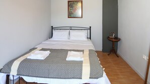 A neatly made bed with a patterned bedspread and pillows, a small bedside table with a decorative item, and a painting on the wall. - 2-bedroom villa in Maroulas Rethymno Villa Pnoi (RETHYMNO)