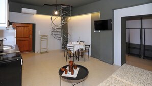 A compact kitchen with a refrigerator, stove, and sink. There's a dining area with a table and chairs, and a spiral staircase leading to an upper level. - 2-bedroom villa in Maroulas Rethymno Villa Pnoi (RETHYMNO)