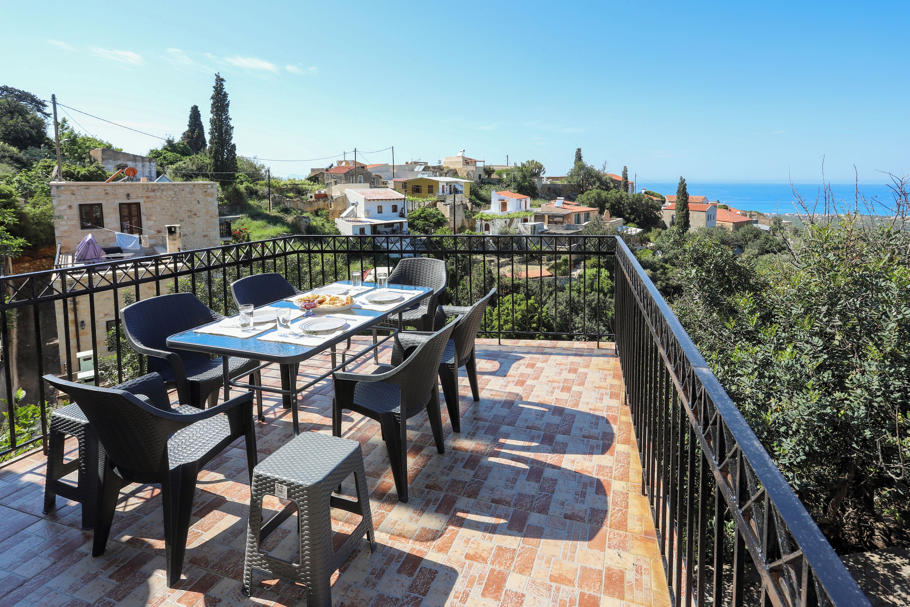 Eine Terrasse mit Tisch und Stühlen mit Blick auf eine Küstenstadt, Häuser und das Meer.