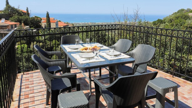 A terrace with a table set for two, overlooking a coastal view. - 2-bedroom villa in Maroulas Rethymno Villa Pnoi (RETHYMNO)