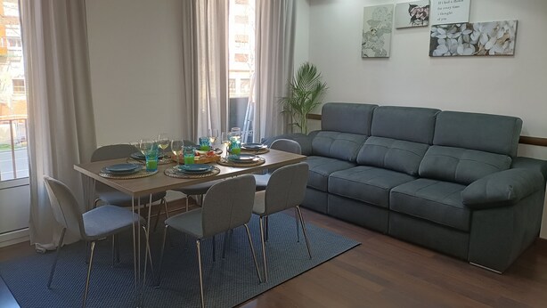 Ein Essbereich mit einem Tisch für vier Personen, einem grauen Sofa und zwei Wandbildern.