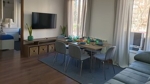 Ein modernes Wohnzimmer mit Essbereich, einem Flachbildfernseher, einer Couch und Blick ins Freie.
