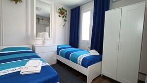 Ein Schlafzimmer mit zwei Betten, einem Kleiderschrank, einem Spiegel und einem Fenster mit Vorhängen.