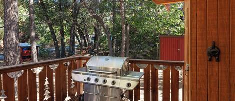 Een roestvrijstalen barbecue op een terras met houten balustrade en een rode schuur op de achtergrond.